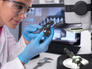 Engineer measuring manufactured component for accuracy and quality control using a dial caliper, 3D stereo microscope in background Engineer measuring manufactured component for accuracy and quality control using a dial caliper, 3D stereo microscope in background